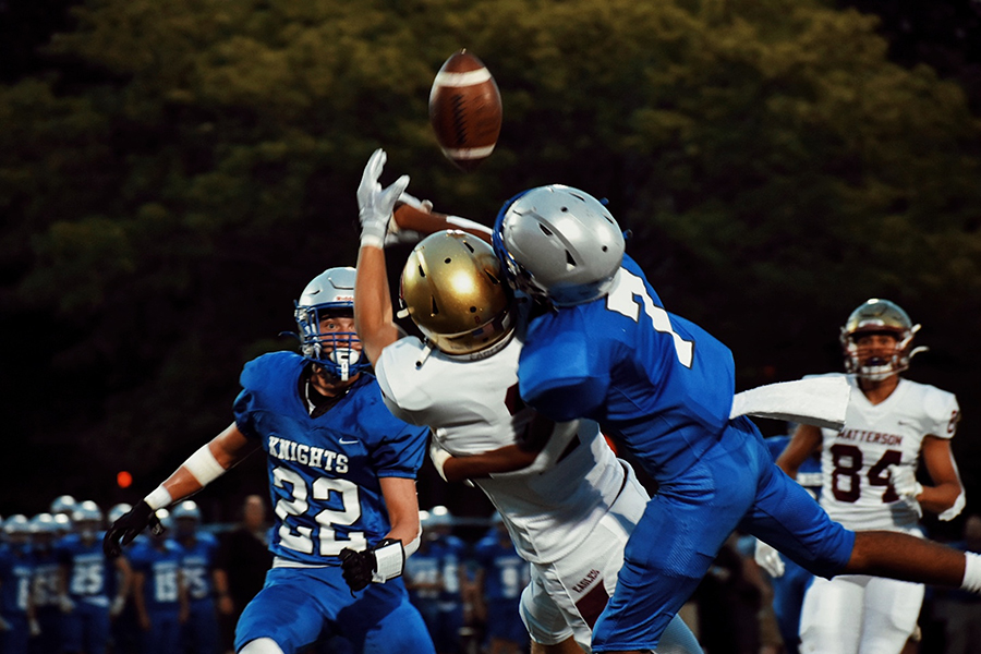 A football player trying to catch the ball as they're being tackled by another playing.