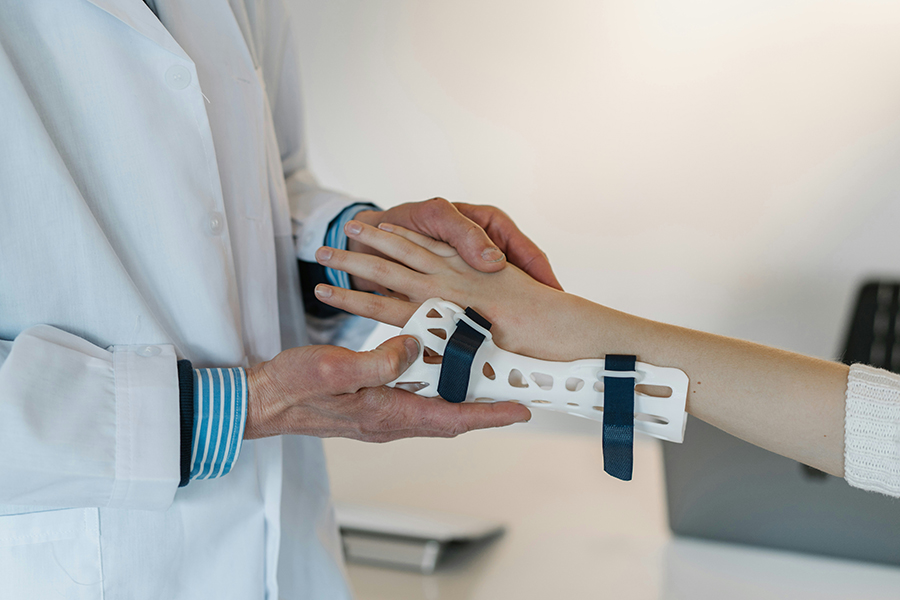 A person in a white coat holding another person's hand while putting on a white cast with black velcro attachments.